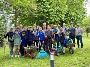 Gruppenfoto der Helfer des SKNL bei einem Arbeitseinsatz im Freien mit Gartengeräten und Schubkarren auf einer Wiese unter Bäumen.