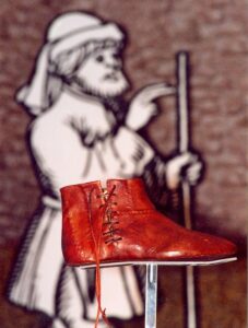 Nachbildung eines historischen Lederschuhs vor Illustration von Bauernführer Joß Fritz.