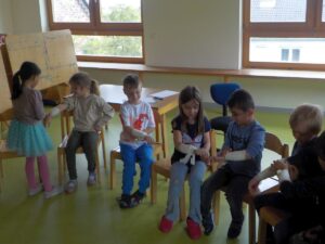 Kinder im Vorschulalter üben Erste Hilfe, indem sie sich gegenseitig Verbände anlegen, in einem Gruppenraum des Kindergartens.