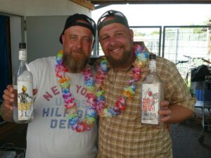 Zwei Männer mit Blumenketten halten Flaschen mit Williams-Birnenbrand und Waldhimbeergeist beim Gockelfest in St. Ilgen in der Hand.