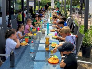 Kinder und Trainer sitzen beim Mittagessen auf der Clubterrasse.
