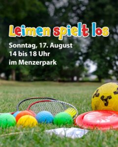 Outdoor-Spielgeräte wie Bälle, Schläger und Frisbee liegen auf einer Wiese, im Hintergrund Bäume im Menzerpark.