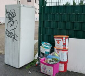 Kühlschrank mit Graffiti und Farbreste an einer Hauswand mit grünem Zaun