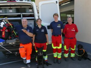 Vier Mitglieder der Wasserrettung mit zwei Rettungshunden vor einem Einsatzfahrzeug.