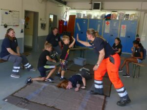 Kinder üben die stabile Seitenlage mit Unterstützung von DRK-Helfer*innen.