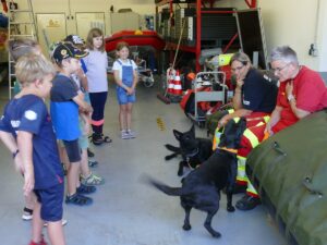 Zwei Rettungshunde und ihre Hundeführerinnen im Gespräch mit einer Gruppe neugieriger Kinder.