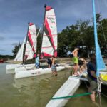 Jugendliche steigen auf Katamarane am Seeufer mit bunten Segeln