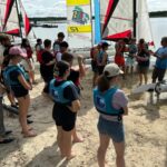Jugendliche hören bei Segelbooten am Strand einem Lehrer zu