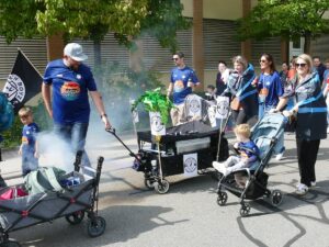 Gruppe in blauen Shirts mit Bollerwagen, Rauch und Kindern beim Kerweumzug in St. Ilgen.