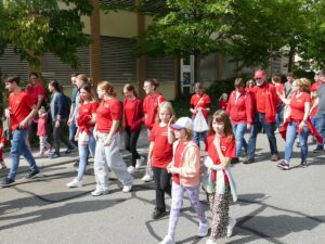 Gruppe in roten T-Shirts und Jacken läuft lachend durch die Straße beim Umzug.