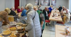 Gäste, hauptsächlich Senioren, sitzen an Tischen im Gastraum der AWO und wählen Kuchen am Buffet.