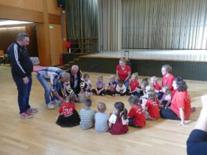 Kinder des TV Germania St. Ilgen sitzen mit Betreuern im Kreis bei Spendenübergabe der Schausteller.