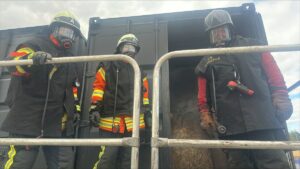 Feuerwehrleute in Schutzkleidung stehen nach der Übung am Container.