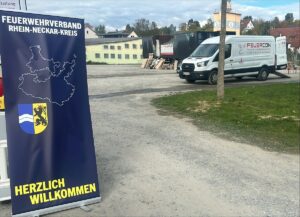 Aufsteller mit Logo des Feuerwehrverbands neben dem mobilen Brandcontainer.
