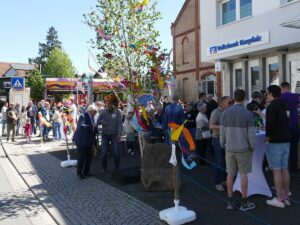 Besucherinnen und Besucher beim Maibaumfest in St. Ilgen vor der Volksbank Kurpfalz mit geschmückter Birke.