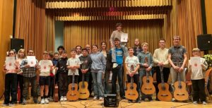 Gruppenfoto von Schülerinnen und Schülern der Musikschule Leimen auf einer Bühne mit Gitarren und Urkunden während der Vorspielwochen 2026.