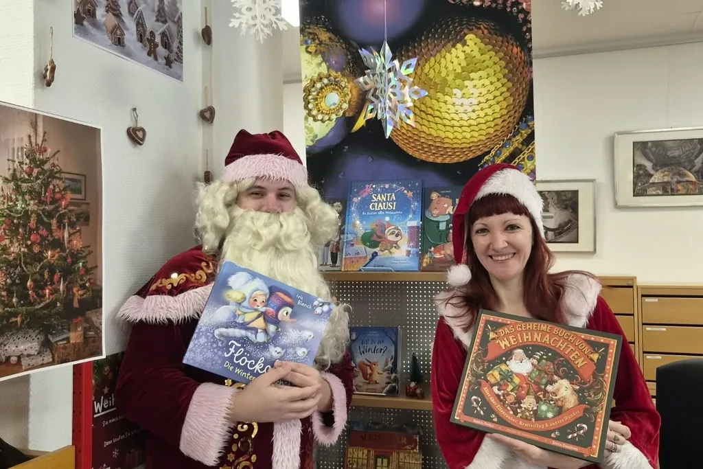 Zwei weihnachtlich gekleidete Erwachsene präsentieren Kinderbücher in der Stadtbücherei Leimen.